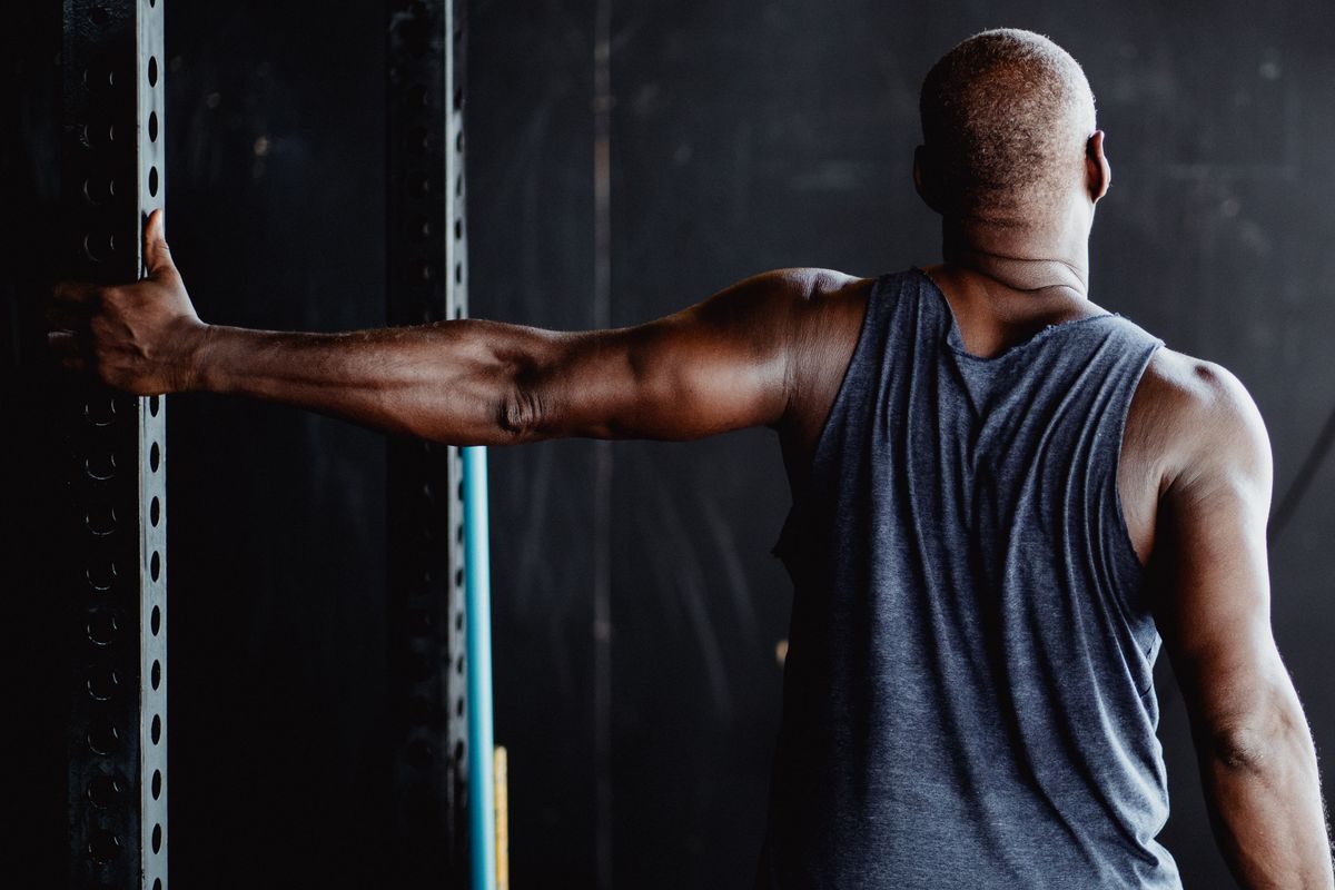Man seen from behind in a dark gym, one hand on the rack