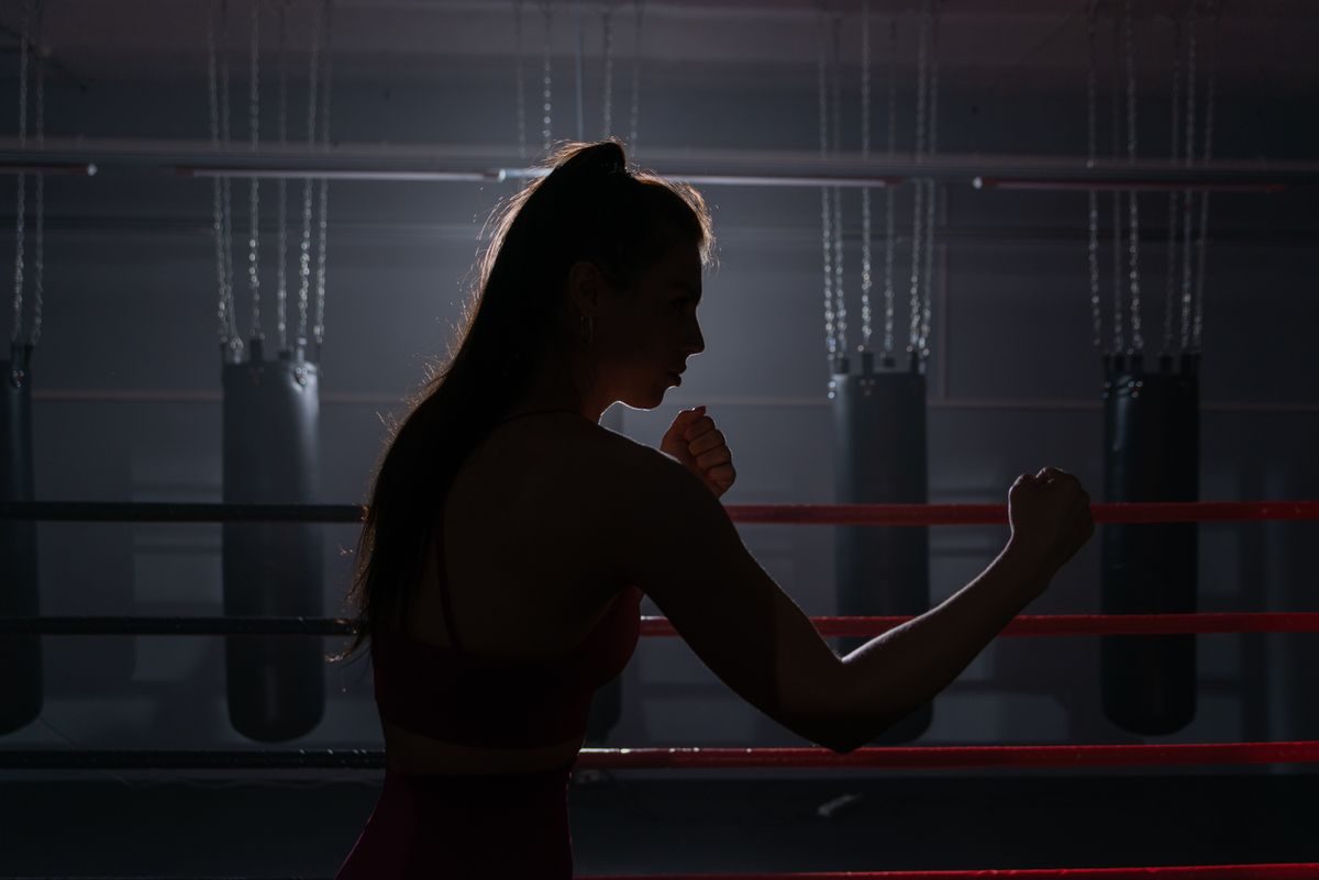 Woman in profile in a dark boxing gym, fists raised